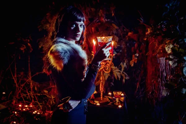 Hermosa bruja con el vaso de vid en el fondo del bosque nocturno . —  Fotos de Stock