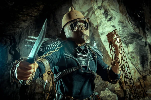 Post-apocalyptic woman in the rusty helmet with a chain and knife in hands on the dungeon background. Nuclear post-apocalypse time. Life after doomsday — Stock Photo, Image