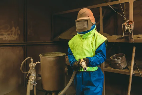 Ein Mitarbeiter bereitet ein Metallteil zum Lackieren vor. Ein strenger Mann arbeitet in der Fabrik. Sandstrahlen. sprengen. — Stockfoto