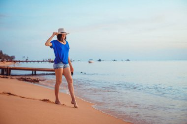 Şapkalı genç bir kadın kumların üzerinde duruyor ve hayal kuruyor..