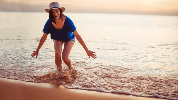 Mujer joven en sombrero está de pie en el mar y riendo . — Foto de Stock