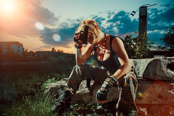 Sexig kvinnlig soldat med pistol vilar. Solnedgång på bakgrunden. — Stockfoto