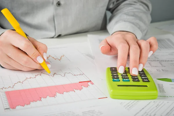 Female hands with pen, black calculator and sheets