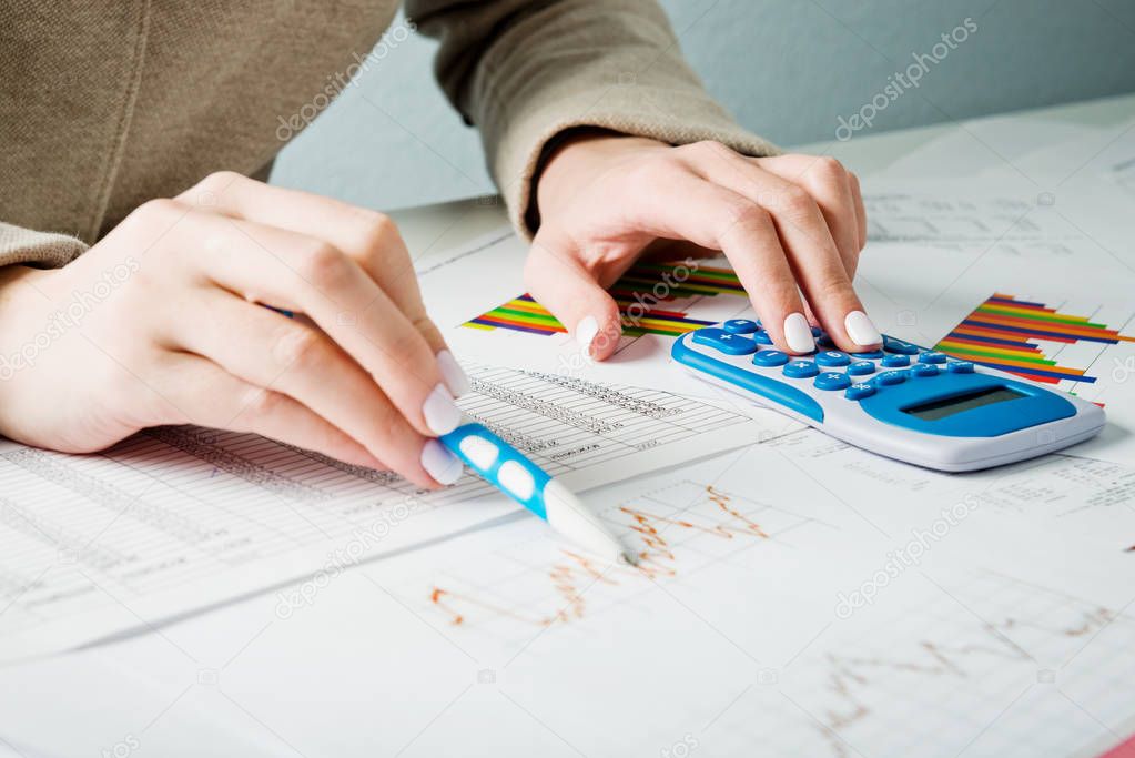 Female hands with pen, blue calculator and sheets