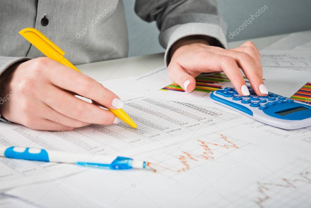 Female hands with pen, blue calculator and sheets