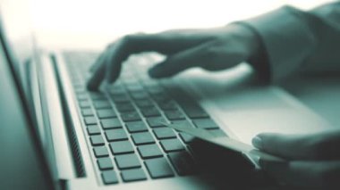 Bir kredi kartı tutan ve online shoppin için dizüstü bilgisayar kullanan eller