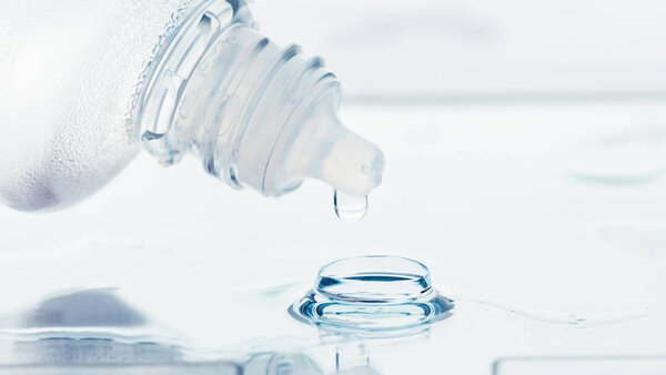 Bottle with lens solution and lens on table