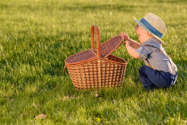 Boy wearing straw hat looking in picnic basket — Stock Photo, Image