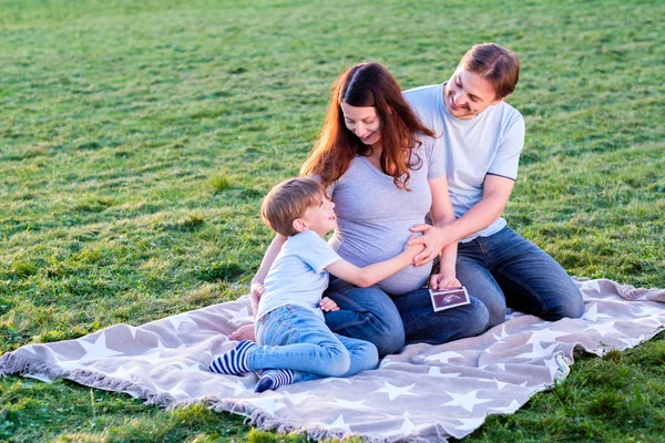 Far och gravid mor med pojke kramar utomhus. — Stockfoto