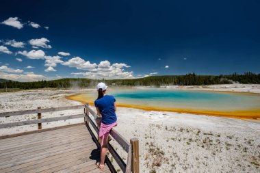 Woman tourist overlooking hot thermal spring Sunset Lake in Yellowstone National Park, Black Sand Basin area, Wyoming, USA clipart
