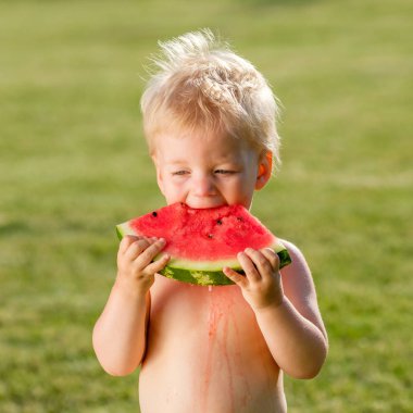 Küçük çocuk karpuz dilimi bahçede yemek ile kırsal sahne. Mutlu bir çocukluk kirli pis yüzü.