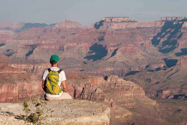 Tourist with backpack at Grand Canyon sitting on the rock edge, Arizona, USA
