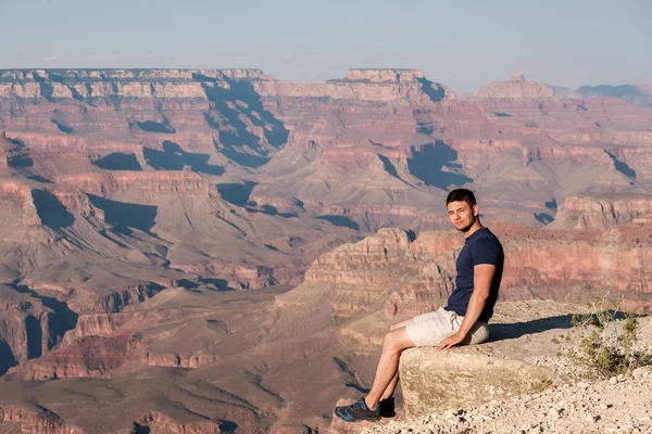 Tourist at Grand Canyon sitting on the rock edge, Arizona, USA