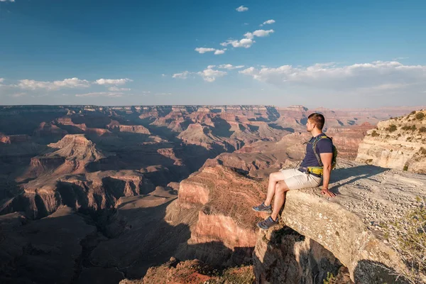 Tourist with backpack at Grand Canyon sitting on the rock edge, Arizona, USA