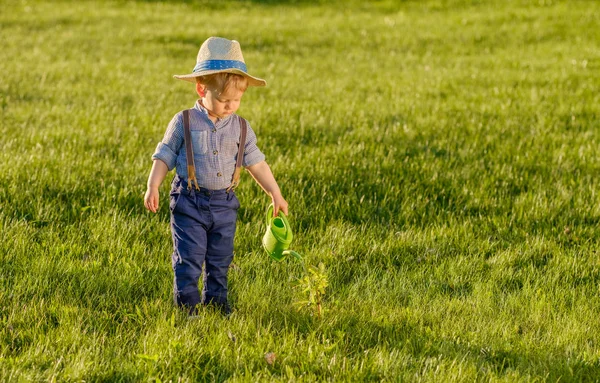 蹒跚学步的孩子在户外的画像 一岁男婴戴草帽使用喷壶的乡村景色 免版税图库图片