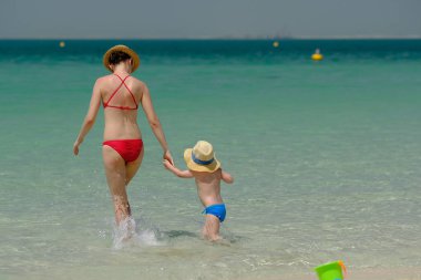 İki yaşındaki yürümeye başlayan çocuk annesi ile Sahilde yürüyüş 