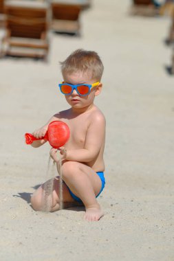 yürümeye başlayan çocuk güneş gözlüğü ile oynarken kürek ve sahilde kum 