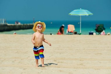 Plajda çalışan güneş şapkalı iki yaşında yürümeye başlayan çocuk 