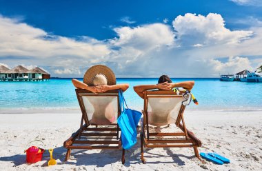 Couple in sun beds on a tropical beach at Maldives clipart