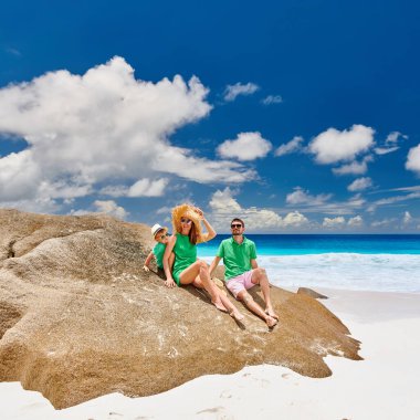Güzel Anse Intendance plajında oturan aile, üç yaşında bir çocukla birlikte yeşil elbiseli genç çift. Seyşeller 'de yaz tatili, Mahe..