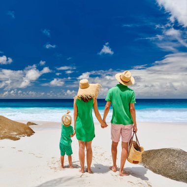 Güzel Anse Intendance plajında bir aile, yeşil elbiseli genç bir çift ve üç yaşında bir çocuk. Seyşeller 'de yaz tatili, Mahe..