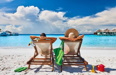 Couple in sun beds on a tropical beach at Maldives clipart