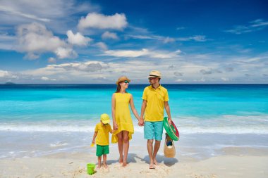 Petite Anse plajında güzel bir aile, üç yaşında bir çocukla sarı elbiseli genç bir çift. Seyşeller 'de yaz tatili, Mahe..