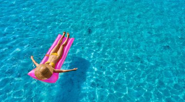 Plajda şişme minder üzerinde dinlenen bir kadın.