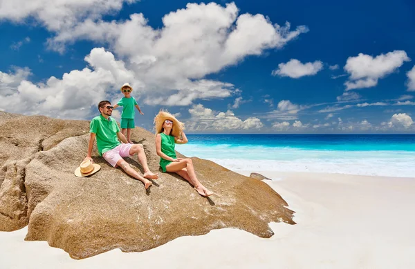 Family sitting on rock on beautiful Anse Intendance beach, young couple in green with three year old toddler boy. Summer vacation at Seychelles, Mahe.
