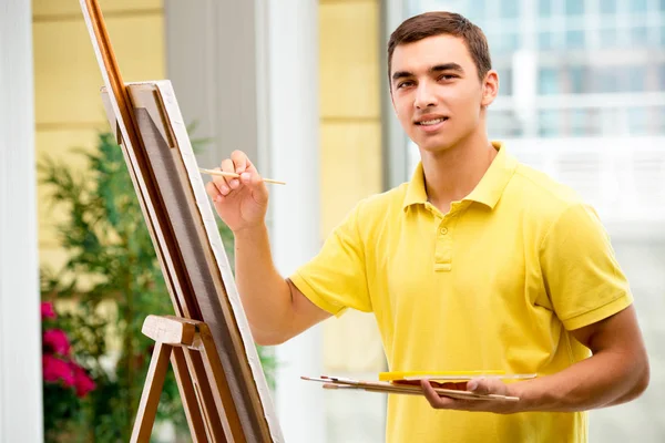 Mladý umělec kreslí obrázky ve světlém studiu — Stock fotografie