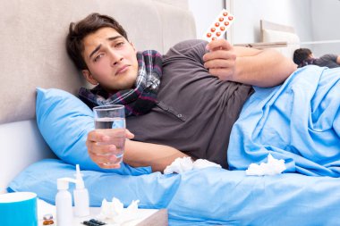 Grip olmuş hasta adam yatakta yatıyor.