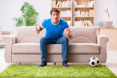 Evdeki kanepede oturup futbol izleyen bir adam.