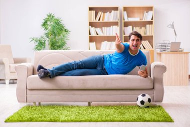 Evdeki kanepede oturup futbol izleyen bir adam.