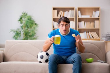Evdeki kanepede oturup futbol izleyen bir adam.