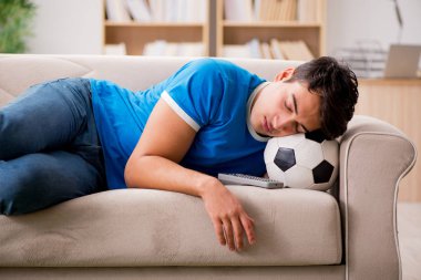 Evdeki kanepede oturup futbol izleyen bir adam.