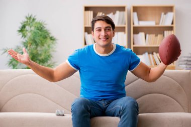 Evdeki kanepede oturup futbol izleyen bir adam.