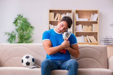 Evdeki kanepede oturup futbol izleyen bir adam.