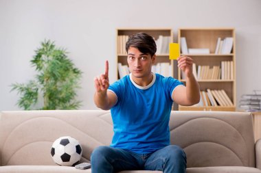 Evdeki kanepede oturup futbol izleyen bir adam.