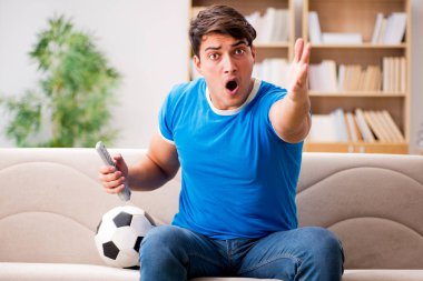 Evdeki kanepede oturup futbol izleyen bir adam.