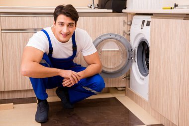 Tamirci mutfakta çamaşır makinesini tamir ediyor.