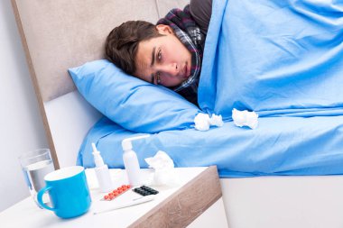 Grip olmuş hasta adam yatakta yatıyor.