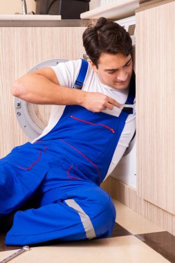 Tamirci mutfakta çamaşır makinesini tamir ediyor.