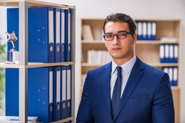 Dosyalarla rafın yanında duran genç adam.