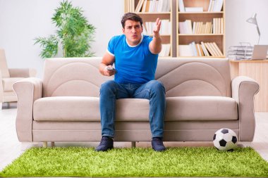 Evdeki kanepede oturup futbol izleyen bir adam.