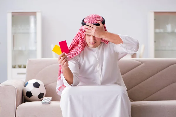 Young arab man watching football sitting on sofa