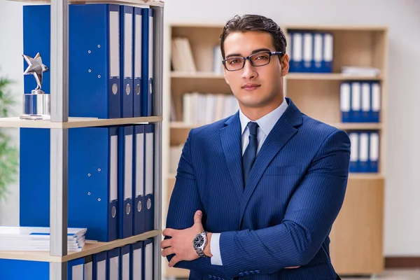 Dosyalarla rafın yanında duran genç adam.