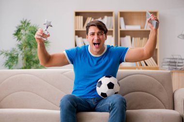 Evdeki kanepede oturup futbol izleyen bir adam.