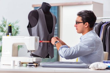 Genç terzi yeni elbiseler üzerinde çalışıyor.