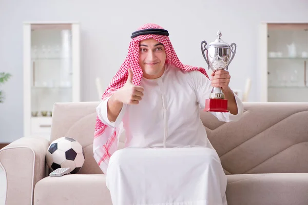 Młody arabski człowiek oglądając piłkę nożną siedzi na kanapie — Zdjęcie stockowe