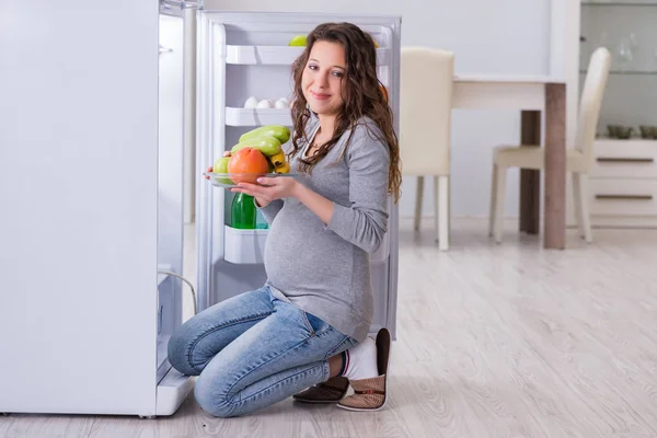 Donna incinta vicino al frigorifero in cerca di cibo e snack — Foto Stock